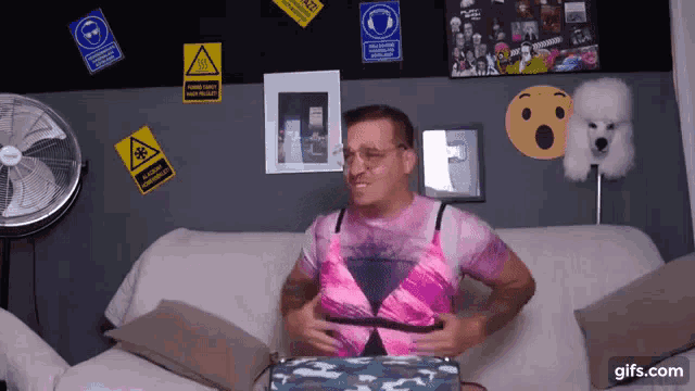 a man is sitting on a couch wearing a pink shirt with a warning sign on the wall behind him