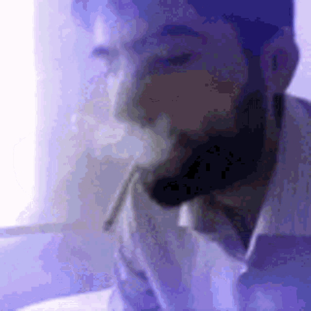 a man with a beard is smoking a cigarette while wearing a white shirt .