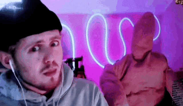 a man wearing headphones and a spongebob costume is sitting in front of a pink neon sign .
