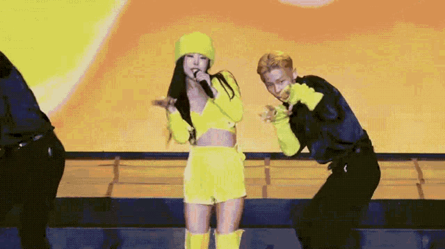 a woman in a yellow outfit is singing into a microphone next to a man
