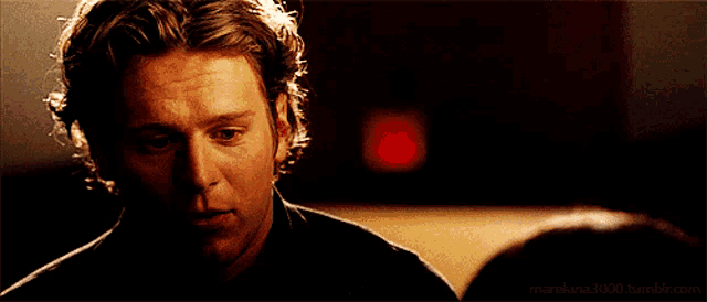 a man in a black shirt is looking at a woman in a dark room with a red exit sign in the background