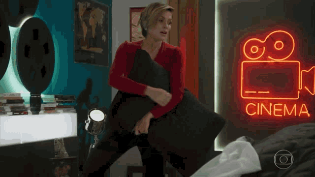 a woman is holding a black pillow in front of a neon sign that says cinema