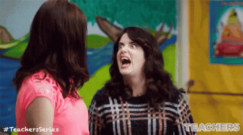 a woman is making a funny face while talking to another woman in a classroom .
