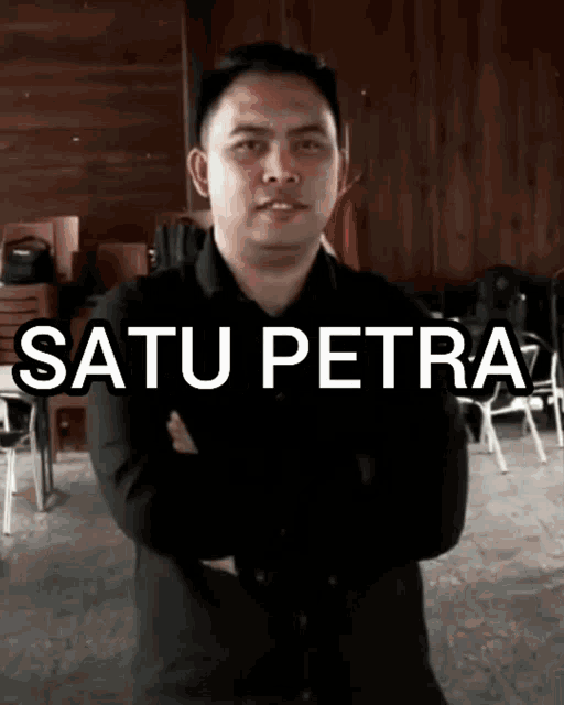 a man stands with his arms crossed in front of a sign that says " satu petra " on it