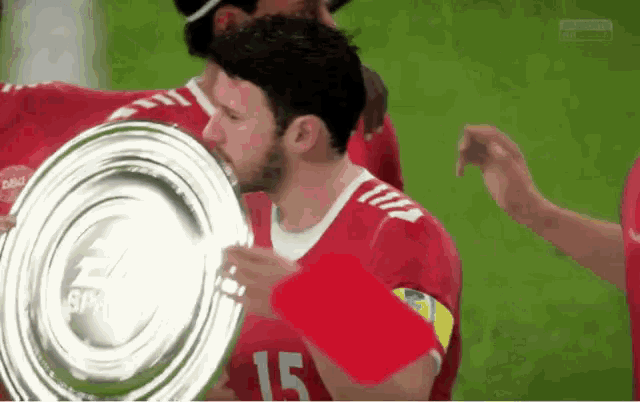 a man in a red jersey with the number 15 on it kisses a trophy