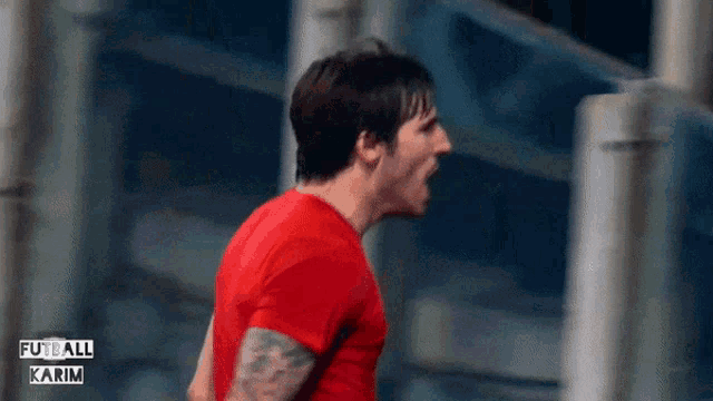 a man in a red shirt is screaming in front of a sign that says futbol karim