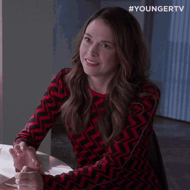 a woman in a red and black sweater sits at a table with her hands folded in front of a youngertv logo