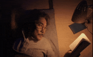 a man wearing glasses is reading a book while laying on a bed