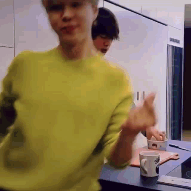 a man in a yellow sweater is dancing in a kitchen next to a cup of coffee .