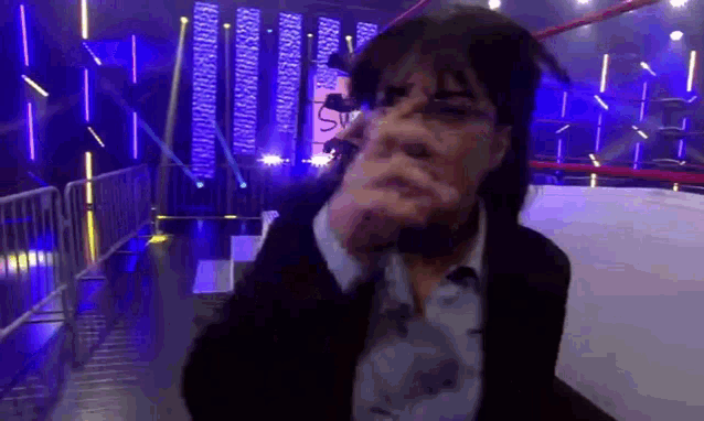 a man in a suit and tie is standing in a wrestling ring covering his face with his hand .