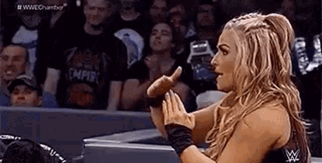 a woman in a wrestling ring is giving a thumbs up while a crowd watches .