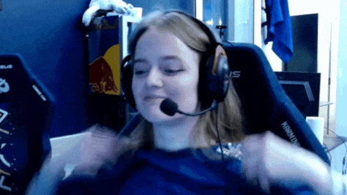 a woman wearing headphones and a microphone is sitting in a chair with a red bull on the wall behind her
