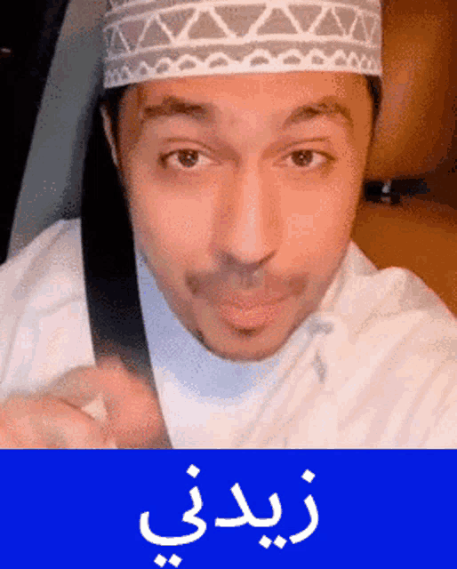 a man wearing a white hat and a seat belt with arabic writing below him