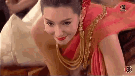 a woman in a red dress and gold jewelry is sitting on a chair .