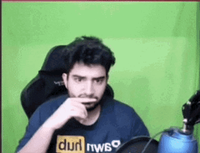 a man with a beard is sitting in front of a green screen wearing a pornhub shirt .