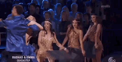 a group of people are dancing in front of a crowd while holding hands .