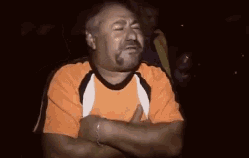 a man with his arms crossed is wearing an orange shirt .