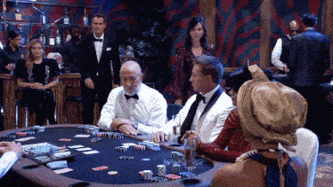 a man in a tuxedo sits at a poker table surrounded by people