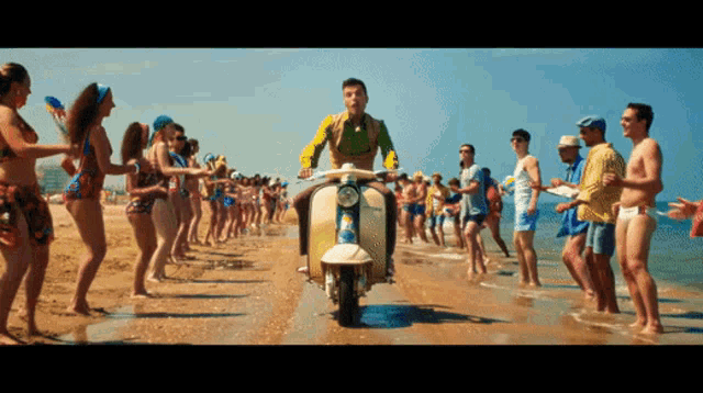 a man riding a scooter on a beach surrounded by people in bikinis