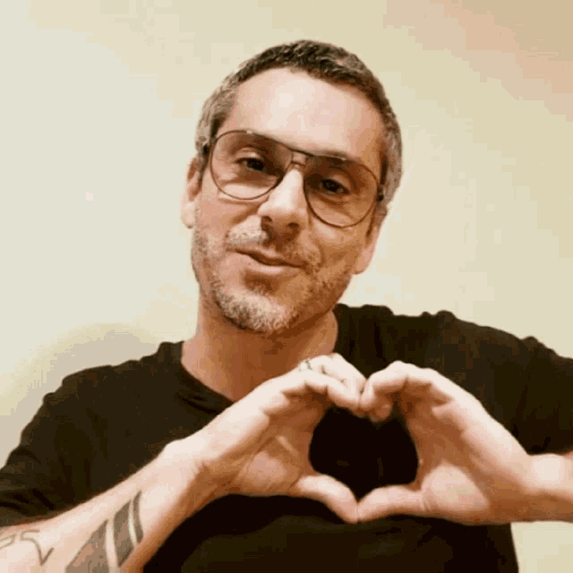 a man wearing glasses makes a heart with his hands