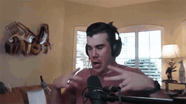 a man wearing headphones and a ring is standing in front of a microphone in a living room .