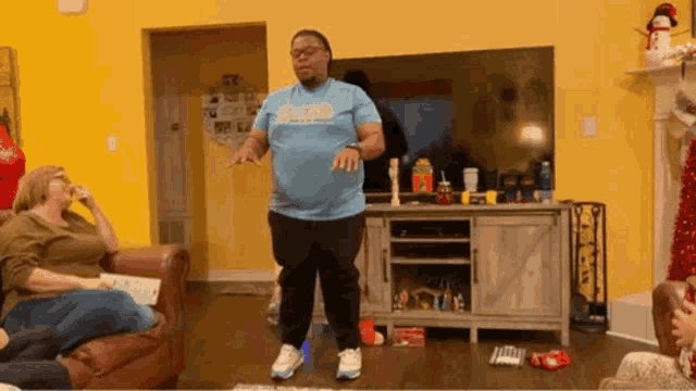a man in a blue shirt is standing in a living room with a woman sitting on a couch .