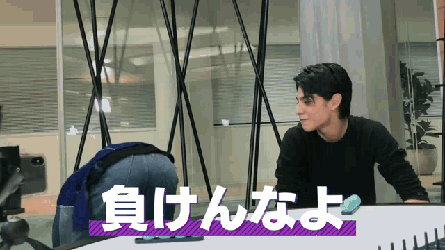 a man in a black sweater is kneeling down in front of a purple sign that says ' 負けんなよ '