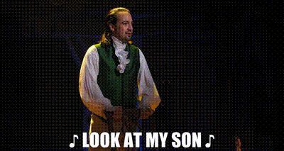 a man in a green vest and white shirt is standing on a stage and says `` look at my son '' .