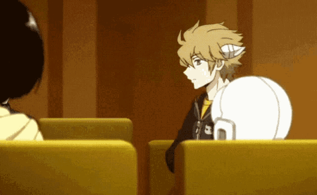a man with a helmet on his head is sitting in a yellow chair talking to another man .