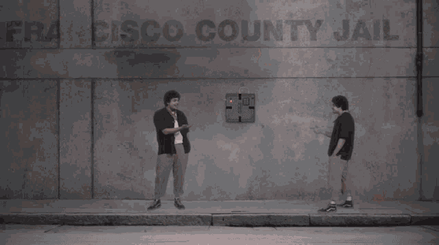 two men standing next to each other in front of a wall with a light coming out of it