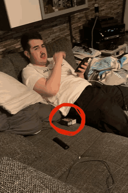 a man laying on a couch holding a cell phone with a red circle around his knee