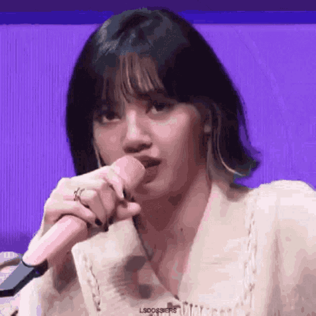 a close up of a woman holding a pink microphone in front of a purple background .