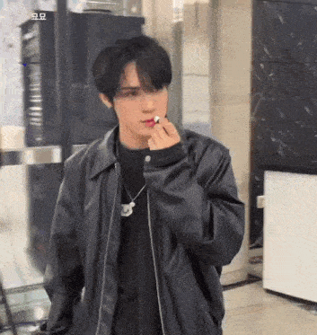 a young man wearing a black leather jacket is smoking a cigarette .