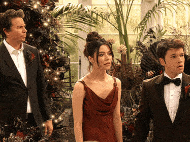 a woman in a red dress is standing next to two men in tuxedos