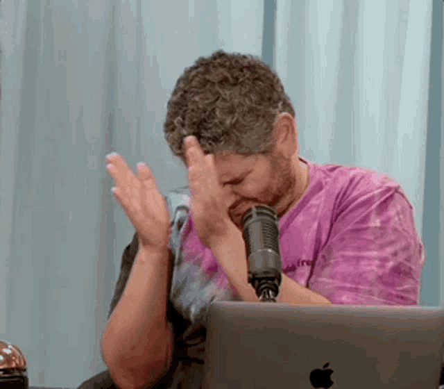 a man in a purple tie dye shirt is sitting in front of a microphone and a laptop computer .