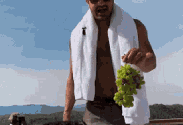 a man with a towel around his neck is holding a bunch of grapes