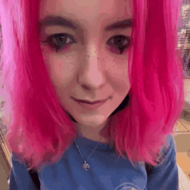 a girl with pink hair is wearing a blue shirt and a necklace .