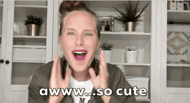 a woman says awww so cute in front of a shelf full of potted plants