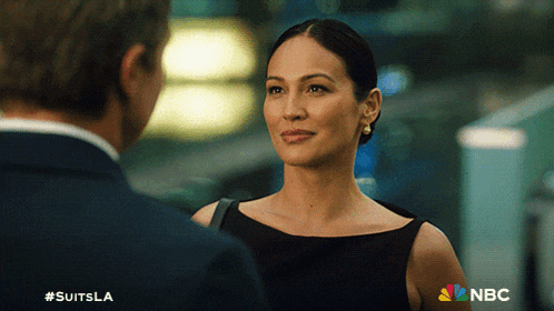 a woman in a black dress is looking at a man in a suit and the nbc logo is visible