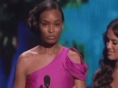 a woman in a pink dress is standing in front of a microphone and making a funny face .