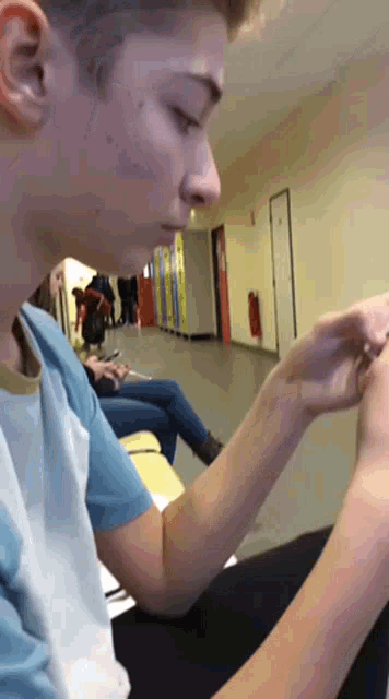 a boy in a blue shirt is sitting in a hallway looking at his phone