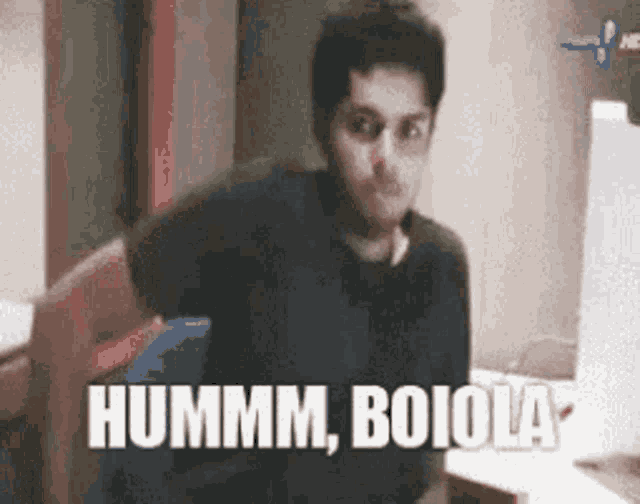 a man is sitting at a desk with the words hummm boiola written on the screen