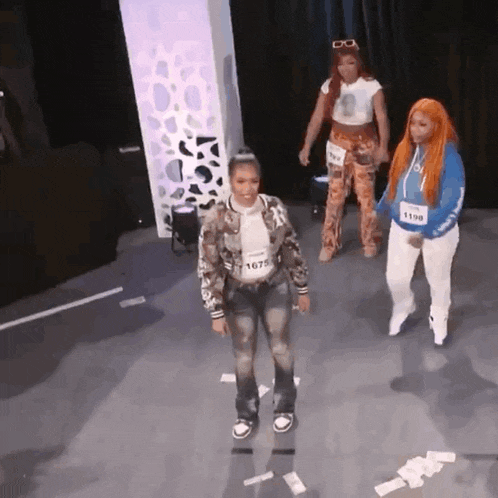 three women are standing on a stage and one has the number 1679 on her waist