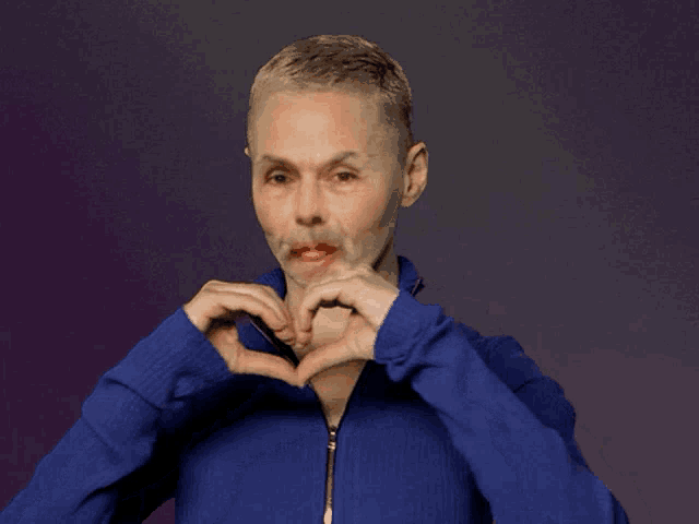 a woman in a blue jacket is making a heart with her hands