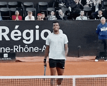 a man stands on a tennis court in front of a sign that says regio ne-rhone-a