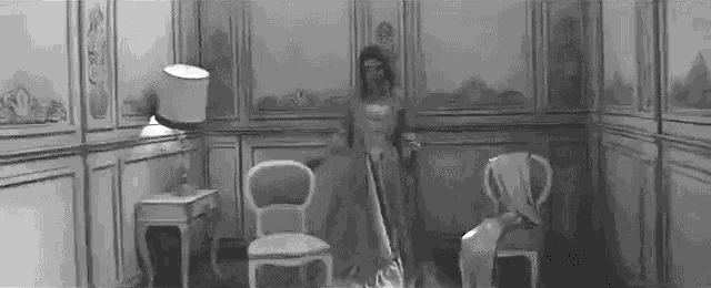 a black and white photo of a woman in a dress vacuuming a room .