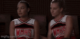 two cheerleaders from glee are sitting next to each other in a room .