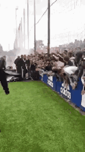 a group of people are standing on a soccer field in front of a fence with the word adidas on it .