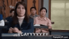 a group of people are sitting at desks in a classroom and one of them is making a funny face .