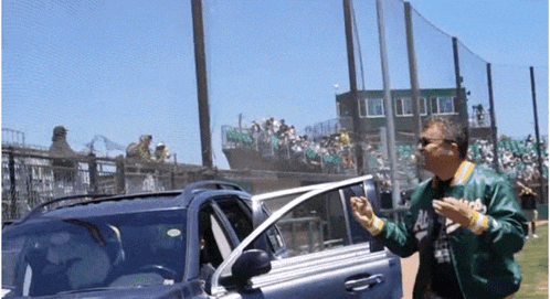a man in a green jacket with the word a's on it stands next to a car